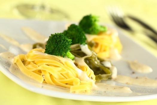 Broccoli florets on yellow and green fettuccine with bechamel sauce and ground pepper (Selective Focus, Focus on the front of the first broccoli floret)