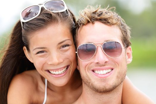 Happy young beach couple closeup portrait outdoors in sun. Young people wearing sunglasses eyewear. Joyful interracial couple, Asian woman, Caucasian man.