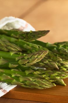 Raw green asparagus wrapped in a dish towel lying on a wooden board (Selective Focus, Focus on the two asparagus heads in the front)