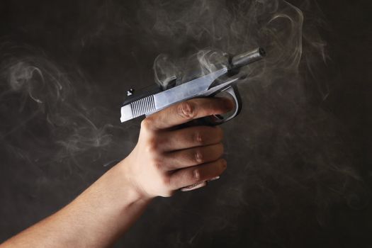 Man's hand a pistol on a dark background with a smoke
