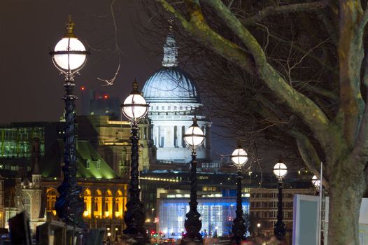 Thames at night. View of St Paul's Cathedral through the cast-iron street lights and tree branches. Buildings on the waterfront lit up. Telephoto shooting