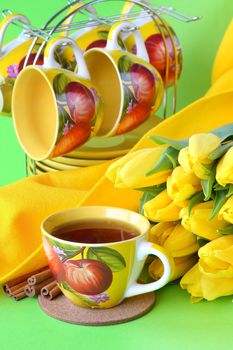 Tea cups and yellow tulips on green background