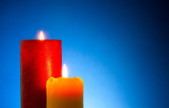 Two burning colourful candles against blue background