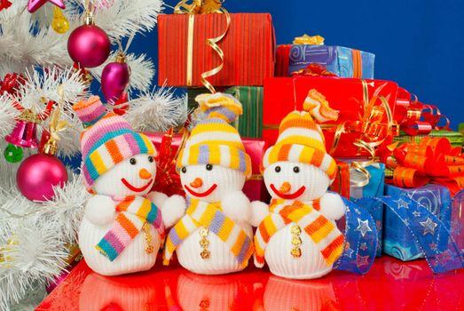 Three snowmen in front of the Christmas presents over the blue background