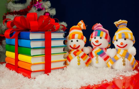 Stack of colorful books tied up with red ribbon and three snowmen