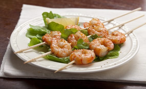 Roasted shrimps on the skewers with lettuce and lemon on the white plate