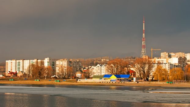 City buildings over the river in bright sunlight, on the other side a dark cloud looming over the city. Khmelnytsky, Ukraine