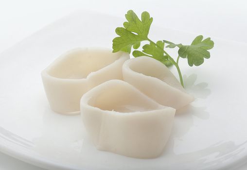 Three raw rings of squid with green parsley on the white plate