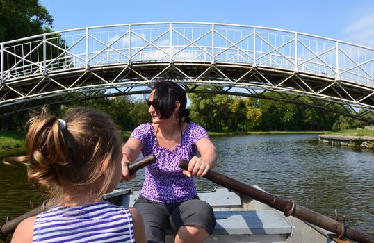 Preschooler girl and her mother ride together in a rowboat on a small fishing lake.