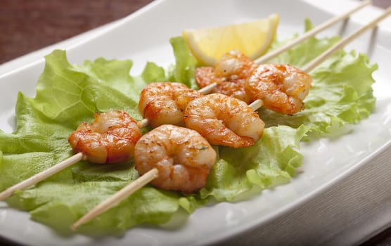 Roasted shrimps on the skewers with lettuce and lemon on the white plate