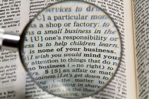 the phrase none of your business in dictionary magnified by handheld magnifying glass