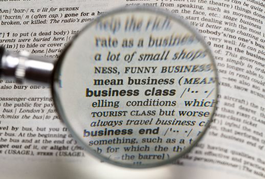 the word business class in dictionary magnified by handheld magnifying glass