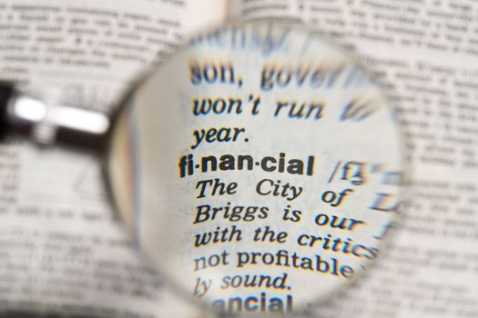 the word financial in dictionary magnified by handheld magnifying glass
