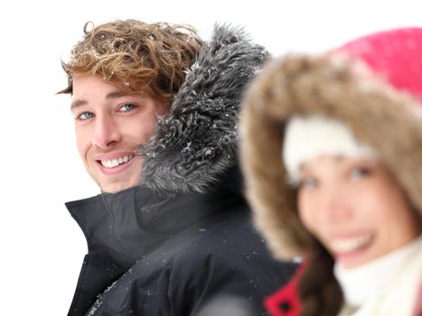 Outdoor couple smiling in winter snow. Focus on Caucasian male model in warm winter clothing. Asian woman, Caucasian male in their 20s.