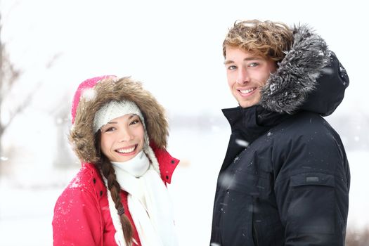 Winter people. Young couple in snow outdoor on winter day. Caucasian man, Asian woman in their twenties.