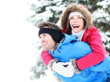 Winter couple piggyback in snow smiling happy and excited. Beautiful young multiracial couple, Asian woman, Caucasian man piggybacking