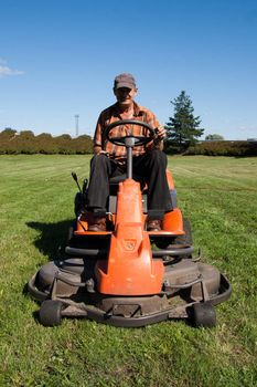 Mature man driving grass cutter in a sunny day