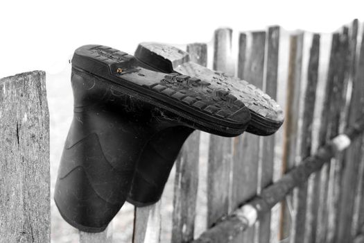 Pair of old rubber boots drying on an old wooden fence