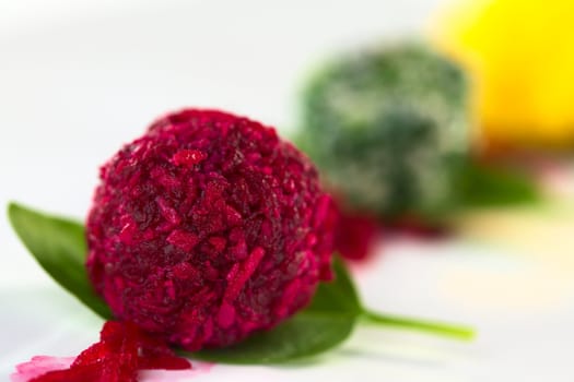 Beetroot, spinach and pumpkin coconut balls on basil leaves (Selective Focus, Focus on the front of the beetroot coconut ball)