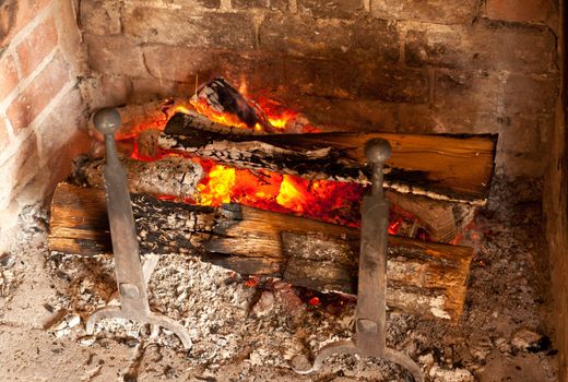 Ancient brick fireplace with wooden logs smouldering