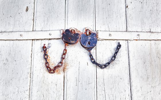 Pair of rusty old padlock and chain fastening a door opening
