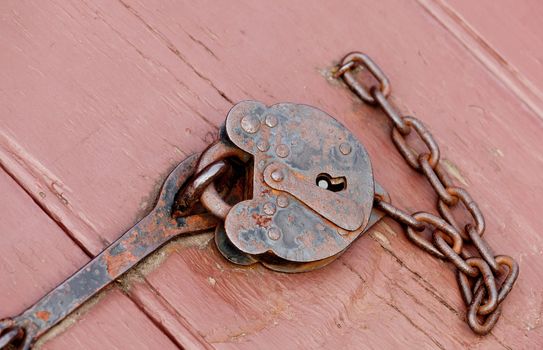 Rusty old padlock and chain fastening a door opening