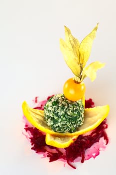 Spinach coconut ball garnished with physalis served on orange peel and grated beetroot (Selective Focus, Focus on the front of the coconut ball and the physalis berry)