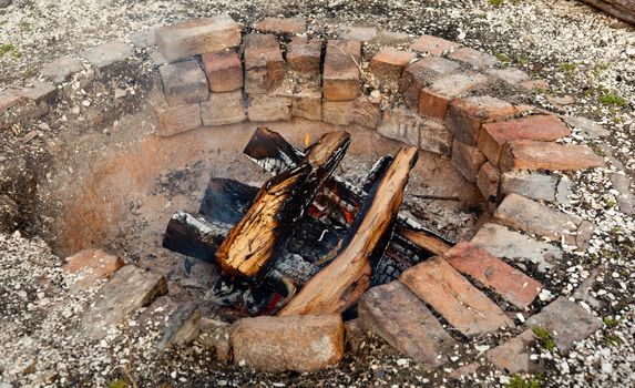 Ancient brick firepit with wooden logs smouldering