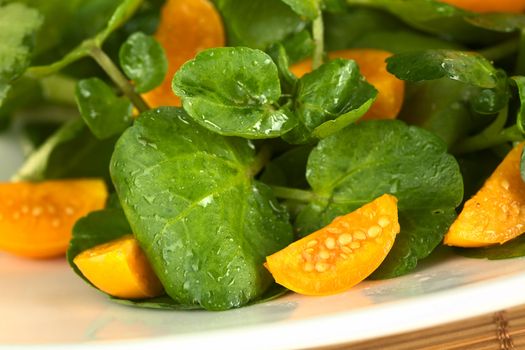 Fresh and healthy watercress (lat. Nasturtium officinale) and physalis (lat. Physalis peruviana) salad (Selective Focus, Focus on the physalis piece in the front and parts of the big leaf on the left)