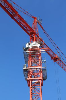 Red building crane against blue sky at site