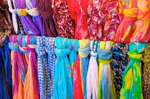 Two rows of brightly colored scarves tied to a rack in a clothing store