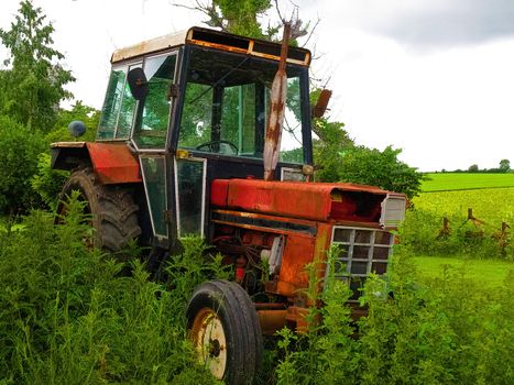 Old rusty red vintage tractor in a farm with green field background digital art manipulation