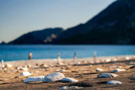 Stones on the sand beach close-up. Background of blurry mountain and sea