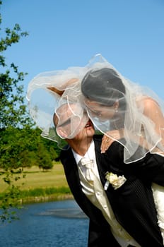 Groom is lifting his bride up in a park.