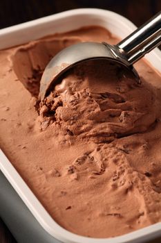 Photo of a metal scoop digging into a tub of chocolate ice cream.