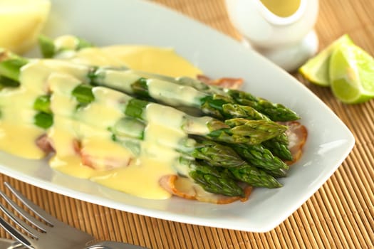 Cooked green asparagus on fried bacon with Hollandaise sauce on top (Selective Focus, Focus on the five asparagus tips in the front)