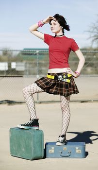 Young alternative woman standing on top of two blue suitcases