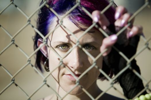 Young woman with colorful hair behind a chain link fence