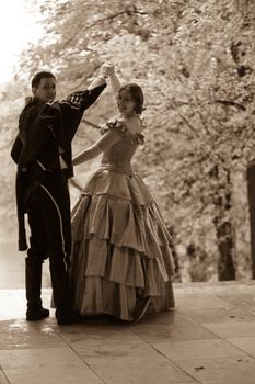 Aged photo: lady and hussar in  XIX century dress in the park 
