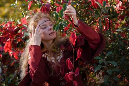 The blonde girle in medieval red dress in the autumn forest
