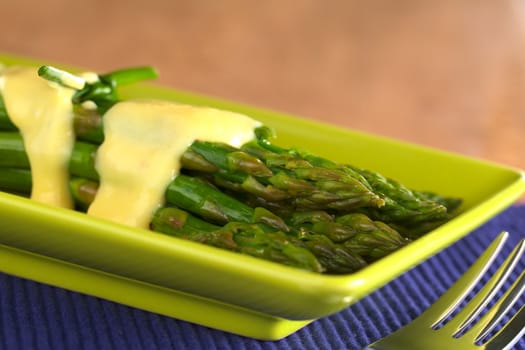 Cooked green asparagus with Hollandaise sauce on top (Selective Focus, Focus on the asparagus tip on the top)