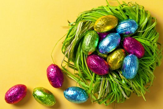 Colorful easter eggs in green nest. Holiday composition on yellow paper background. Top view