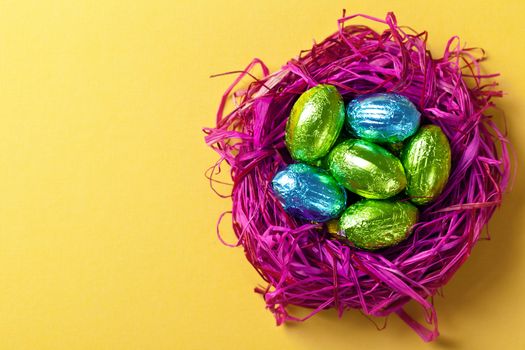 Easter eggs in pink nest. Holiday composition on yellow paper background. Top view. Macro shot