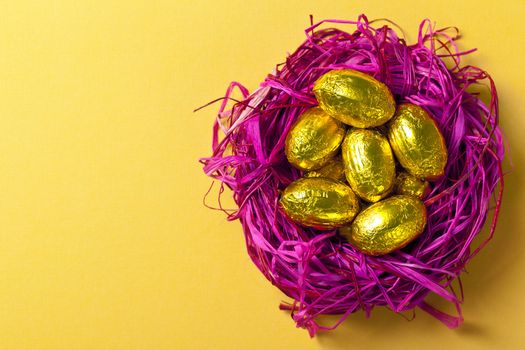Easter eggs in pink nest. Holiday chocolate composition on yellow paper background. Top view. Macro shot