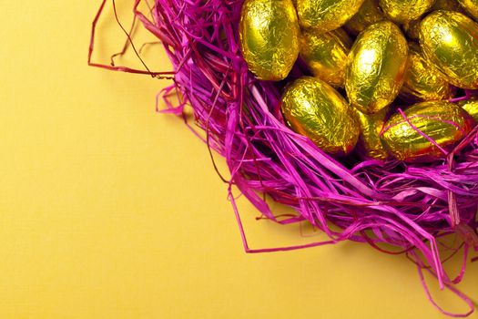 Gold easter eggs in pink nest. Holiday background with sweets. Top view. Macro shot