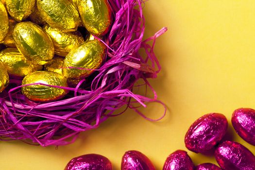 Chocolate easter eggs in pink nest. Holiday background. Selective focus on gold eggs. Top view 