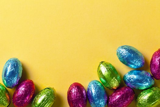 Easter background with colorful chocolate eggs on yellow paper. Top view, macro shot