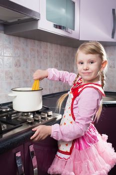 little girl in the kitchen putting pasta in the pot 