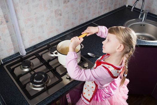 little girl in the kitchen putting pasta in the pot 