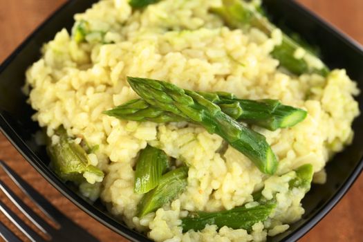 Green asparagus risotto in black bowl (Selective Focus, Focus on the upper asparagus tip)